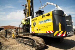 Nahaufnahme eines gelben Bohrgeräts vom Typ Soilmec SR-45, Arbeiter in Schutzkleidung stehen daneben und führen Bohrarbeiten aus.