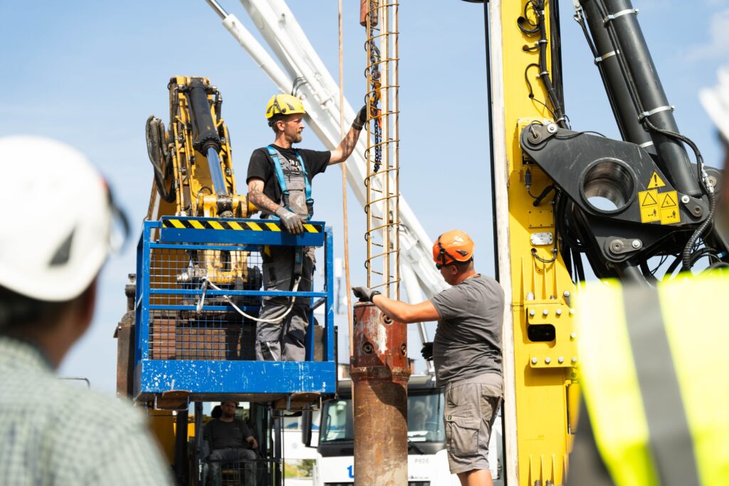 Bauarbeiter führen Bohrarbeiten für eine Tiefgründung mit schwerem Gerät auf einer Baustelle aus.