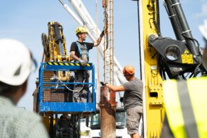 Bauarbeiter führen Bohrarbeiten für eine Tiefgründung mit schwerem Gerät auf einer Baustelle aus.
